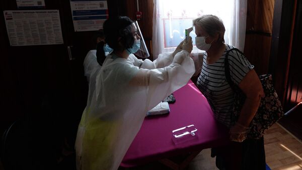 Женщине измеряют температуру при входе на избирательный участок №81 в сельском клубе поселка Усть-Мана Красноярского края, где проводится голосование по внесению поправок в Конституцию РФ 