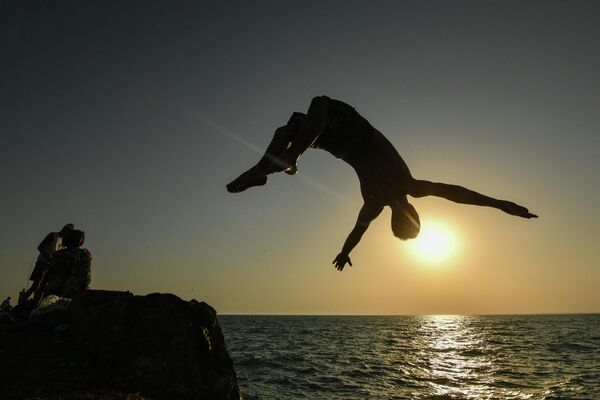 Мужчина прыгает с пирса на пляже в посёлке городского типа Новофёдоровка Сакского района