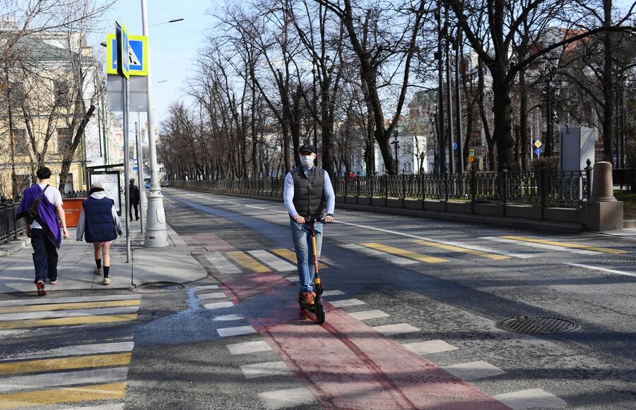 Мужчина в медицинской маске едет на самокате по велодорожке в центре Москвы.