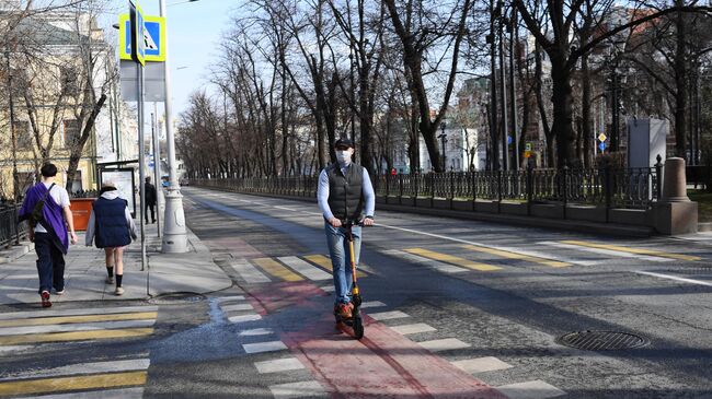 Мужчина в медицинской маске едет на самокате по велодорожке в центре Москвы.