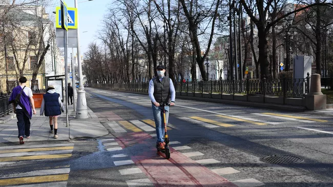 Мужчина в медицинской маске едет на самокате по велодорожке в центре Москвы.