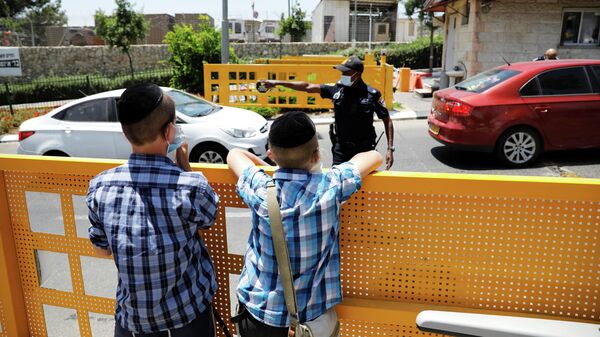 Мальчики смотрят на полицейского, который работает на въезде в еврейское поселение Бейтар-Иллит, закрытое после новых случаев заболевания коронавирусом (COVID-19)