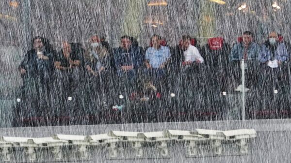Болельщики на трибуне наблюдают во время дождя за ходом матча РПЛ Спартак — Локомотив