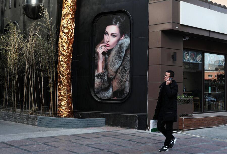 Мужчина у рекламного плаката продажи шуб с русскими моделями в торговом районе для русских Ябаолу в Пекине