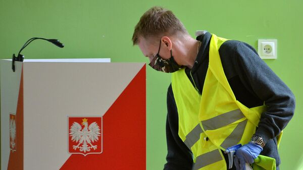 Сотрудник избирательной комиссии проводит дезифекционную обработку кабинок во время голосования на выборах президента Польши