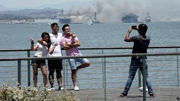 Люди фотографируются на фоне горящего универсального десантного корабля USS Bonhomme Richard (LHD 6)
