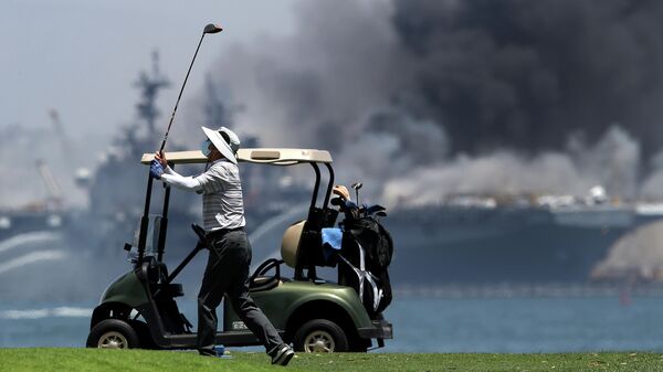Мужчина играет в гольф на фоне горящего универсального десантного корабля USS Bonhomme Richard (LHD 6)