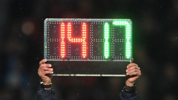 Арбитр держит табло, символизирующее о замене футболистов