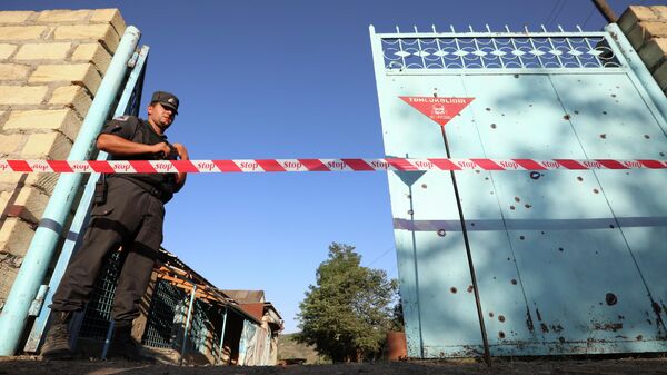 Сотрудник правоохранительных органов охраняет двор с не взорвавшимся снарядом после обстрела со стороны Армении в деревне Агдам, Азербайджан