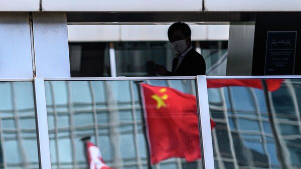 Мужчина на пешеходном мосту, в котором отражается флаг Китая, Гонконг