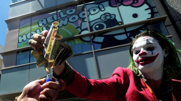 Участник акции протеста против политики Дональда Трампа в костюме Джокера сжигает долларовые банкноты на Аллее славы в Голливуде, США
