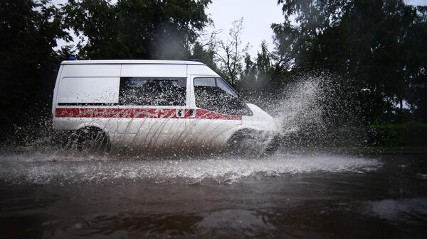 Автомобиль скорой помощи едет по подтопленной после дождя дороге в Москве