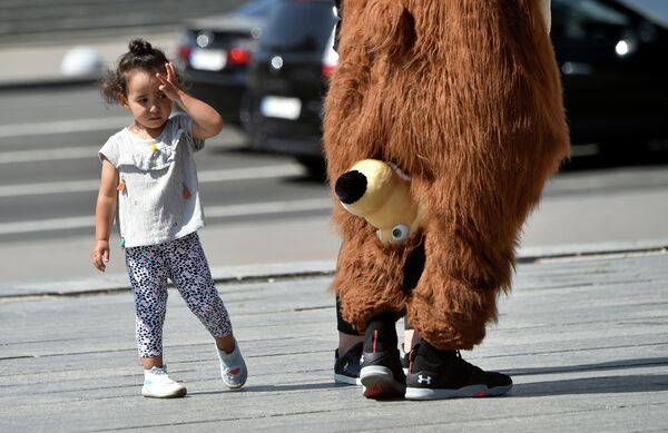 Девочка смотрит на уличного артиста в костюме медведя в Киеве, Украина