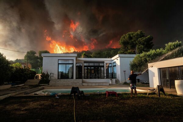 Мужчина поливает свой дом из шланга прежде чем покинуть его из-за наступающего лесного пожара в Ла-Куроне, Франция 
