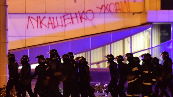 Сотрудники правоохранительных органов проходят мимо здания с надписью Лукашенко уходи! во время массовой акции протеста после президентских выборов в Минске, Беларусь