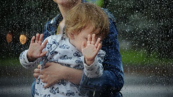 Женщина с ребенком на остановке общественного транспорта в Москве во время дождя