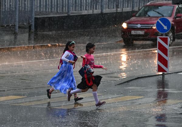 Девочки перебегают через дорогу во время сильного дождя в Москве