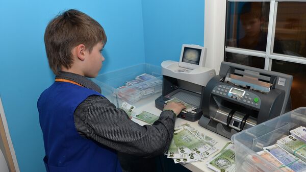 Мальчик проверяет подлинность банкнот на специальной аппаратуре в Детском банке