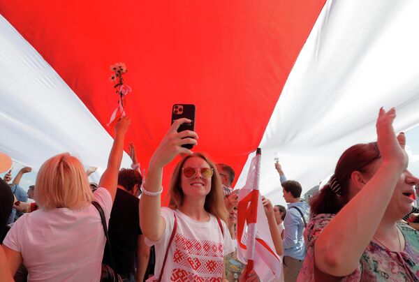 Демонстранты держат гигантский бело-красно-белый флаг Беларуси во время акции протеста против результатов президентских выборов в Минске, Беларусь