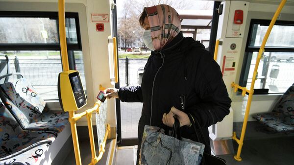 Женщина прикладывает социальную карту к валидатору в салоне городского автобуса