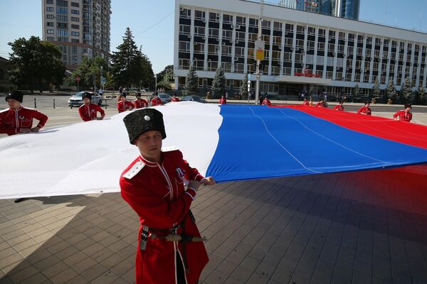 Казаки почётного караула Кубанского казачьего войска разворачивают триколор на Главной городской площади Краснодара во время празднования Дня Государственного флага РФ