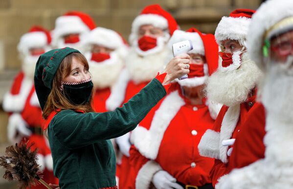 Женщина в костюме эльфа измеряет температуру посетителям школы Санта-Клауса в Лондоне, Великобритания