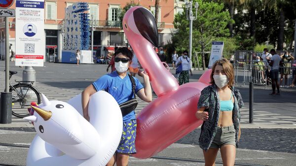Отдыхающие в защитных масках идут на пляж в Ницце 