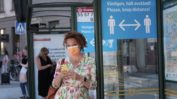 Женщина в защитной маске на автобусной остановке с плакатом, призывающим держать социальную дистанцию, Стокгольм, Швеция