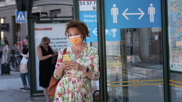 Женщина в защитной маске на автобусной остановке с плакатом, призывающим держать социальную дистанцию, Стокгольм, Швеция