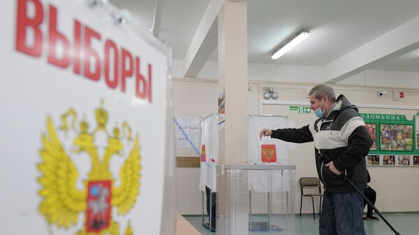 Мужчина опускает бюллетень в урну на избирательном участке