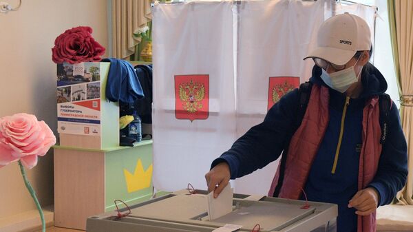 Девушка опускает бюллетень в урну на избирательном участке во время выборов губернатора Ленинградской области