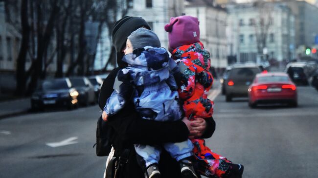 Женщина с двумя детьми на руках переходит дорогу.