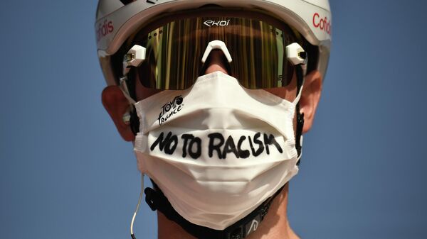 Велогонщик на этапе Тур де Франс в защитной маске, на которой написан лозунг против расизма