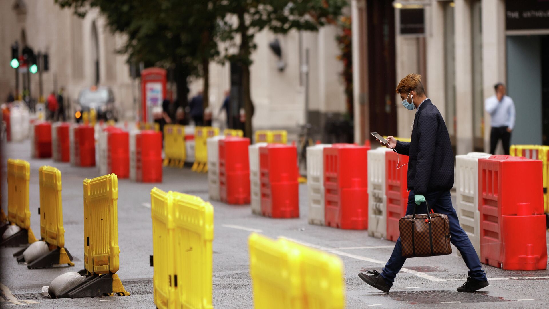Мужчина в защитной маске переходит дорогу с установленными на ней барьерами для социального дистанцирования в Лондоне - РИА Новости, 1920, 15.10.2020
