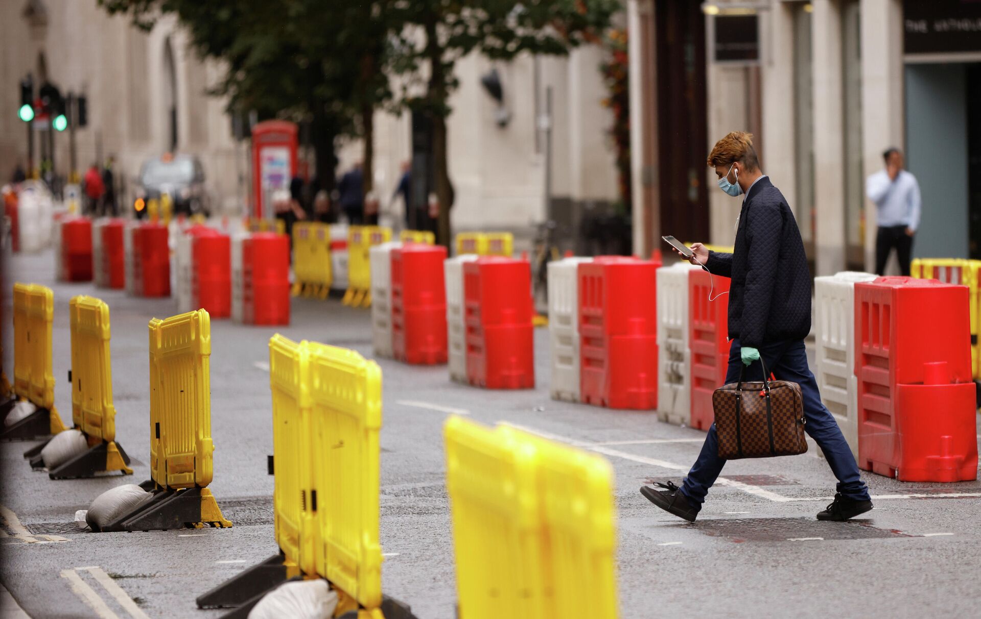 Мужчина в защитной маске переходит дорогу с установленными на ней барьерами для социального дистанцирования в Лондоне - РИА Новости, 1920, 24.09.2020