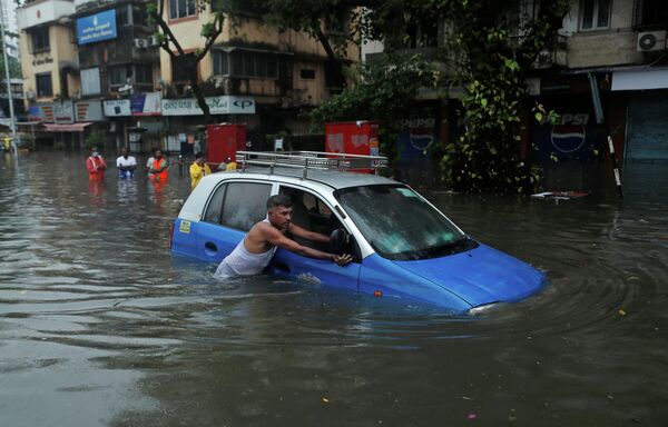 Мужчина толкает такси по затопленной улице после ливня в Мумбаи, Индия