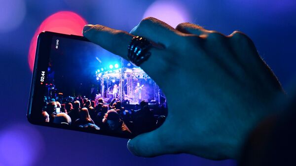 Зритель снимает на мобильный телефон выступление музыкантов на концерте