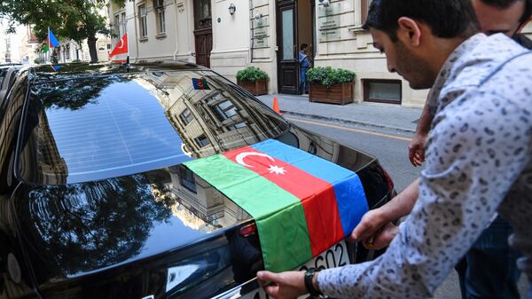 Житель Азербайджана прикрепляет флаг Азербайджана на автомобиль