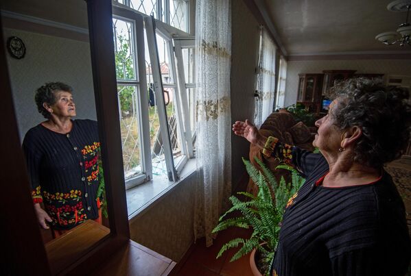 Женщина показывает выбитые окна в результате обстрелов общины Иванян Нагорного Карабаха