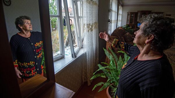 Женщина показывает выбитые окна в результате обстрелов общины Иванян Нагорного Карабаха