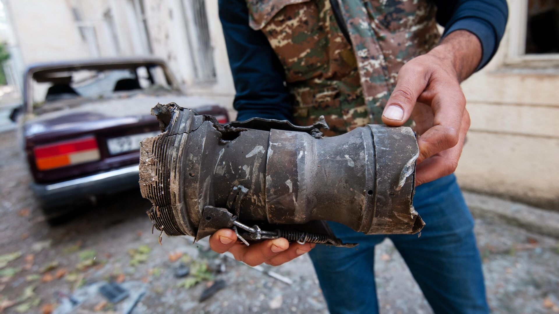 Мужчина держит в руках осколок от разорвавшегося снаряда в результате обстрела на одной из улиц города Мартуни - РИА Новости, 1920, 14.10.2020