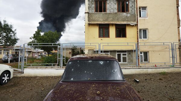 Осколочные пробоины в автомобиле на фоне горящего здания после обстрела в Степанакерте