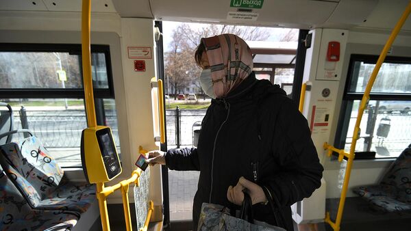 Женщина в защитной маске прикладывает социальную карту к валидатору в салоне автобуса