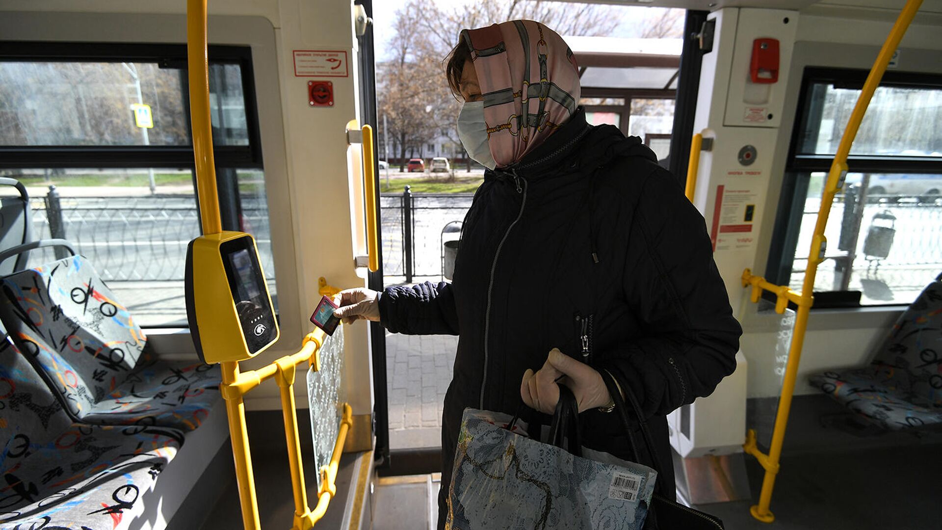 Женщина в защитной маске прикладывает социальную карту к валидатору в салоне автобуса - РИА Новости, 1920, 05.10.2020