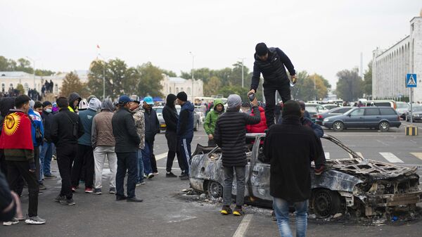 Протестующие у сожженного автомобиля на центральной площади Бишкека Ала-Тоо