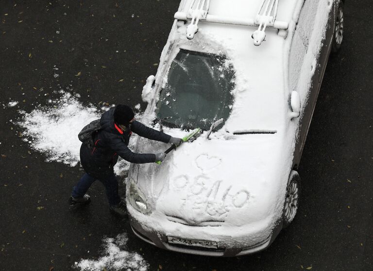 Женщина очищает автомобиль от снега после первого снегопада в городе Дивногорске Красноярского края