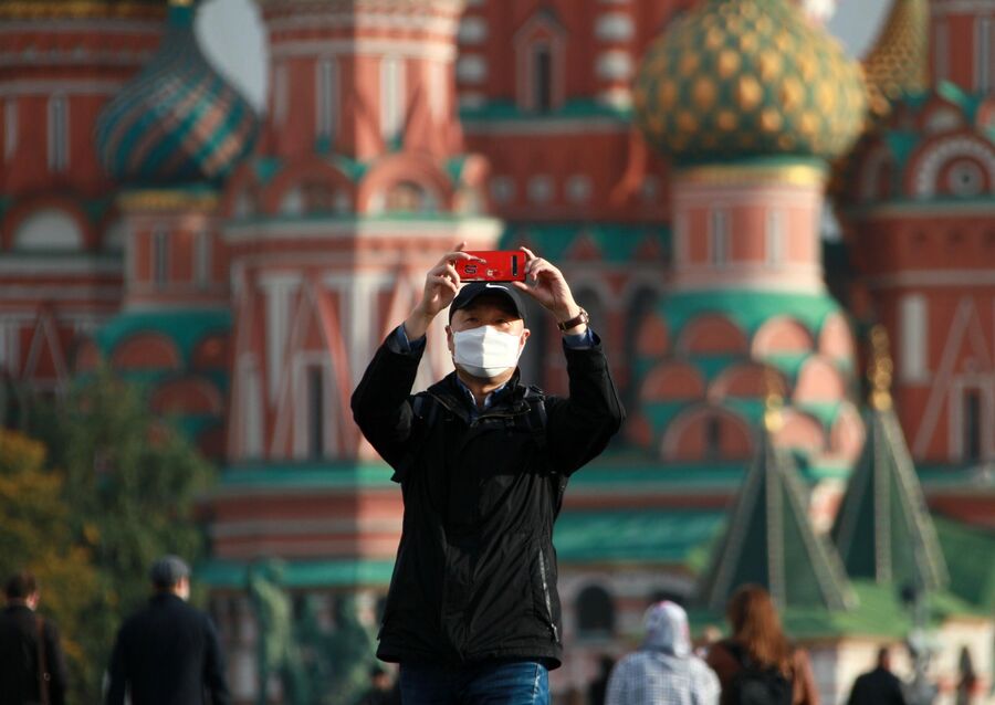 Мужчина в медицинской маске фотографируется около Собора Василия Блаженного на Красной площади в Москве