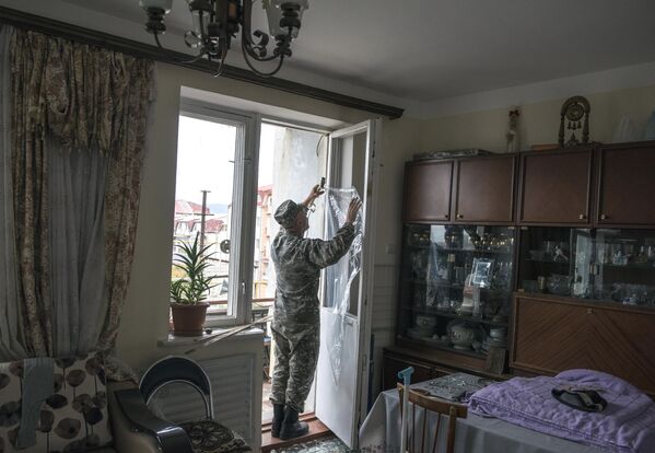 Мужчина закрывает полиэтиленовой пленкой окно с выбитыми стеклами после обстрелов Степанакерта Нагорном Карабахе