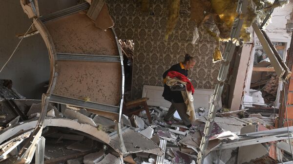 Жительница собирает уцелевшие вещи на развалинах своего жилого дома, разрушенного в результате ракетного обстрела города Гянджа