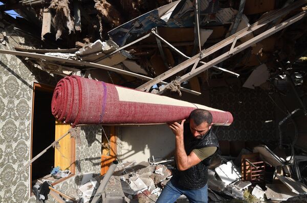 Жители с уцелевшим ковром вещи на развалинах своего жилого дома, разрушенного в результате ракетного обстрела города Гянджа